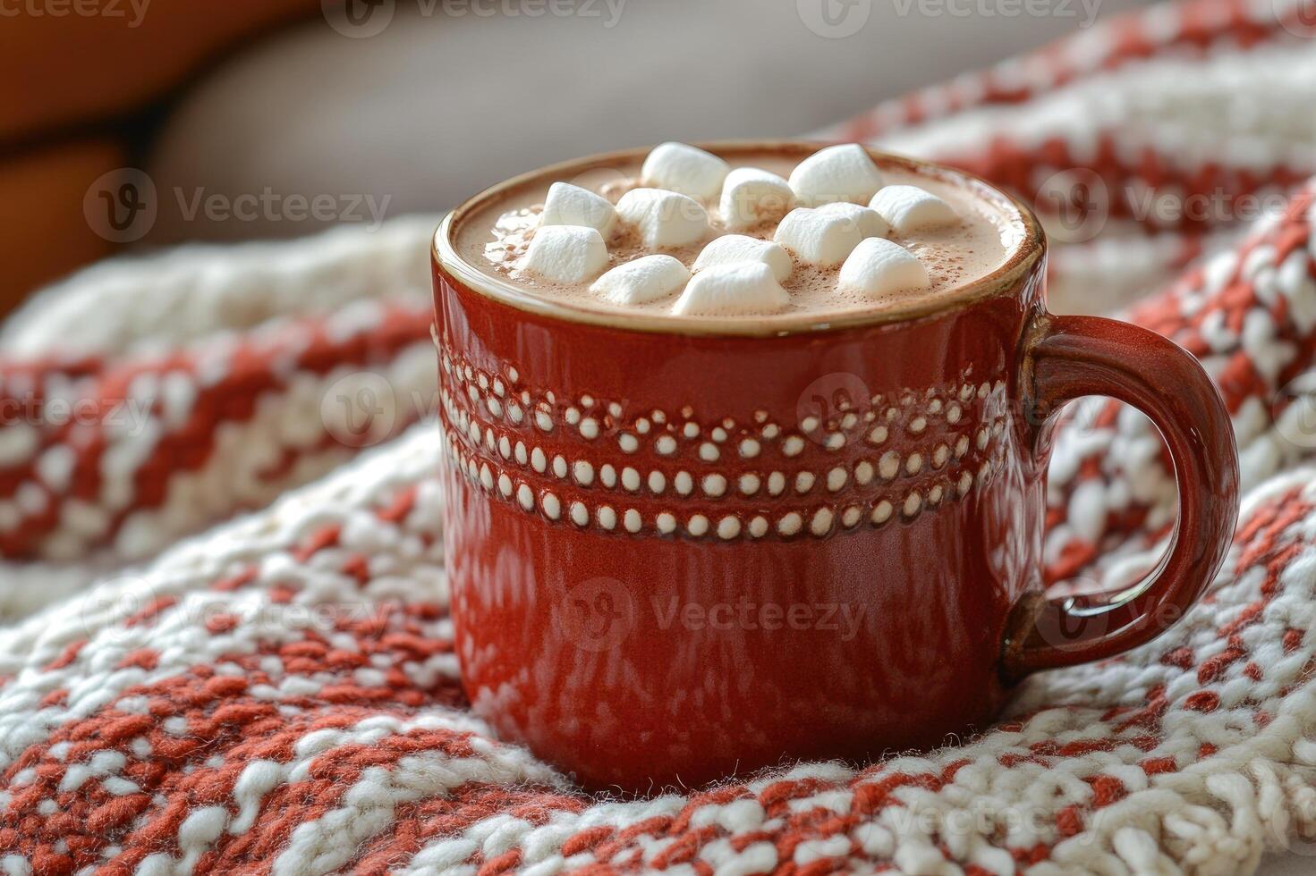 Red mug containing hot chocolate with marshmallows warming on a cozy christmas blanket photo