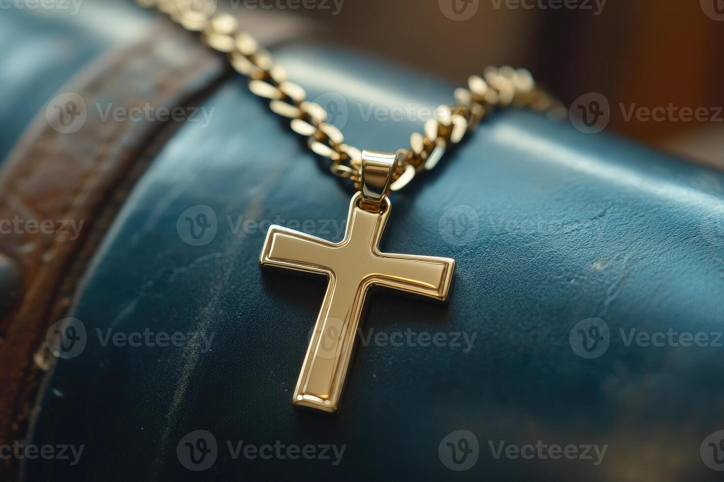 Golden cross pendant hanging on gold chain resting on blue leather surface photo