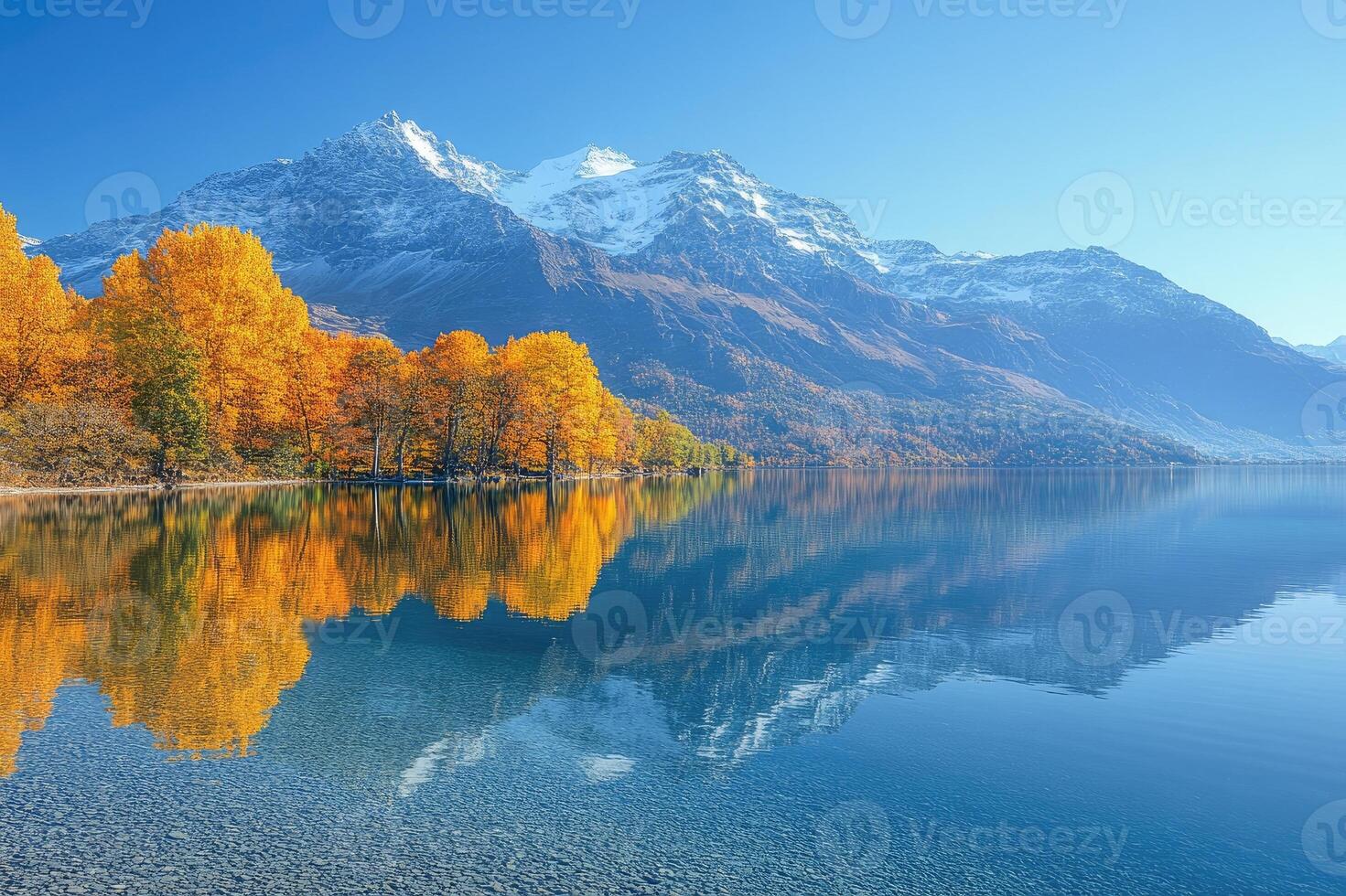 Autumn trees reflecting in a crystal clear lake with snow-capped mountains photo
