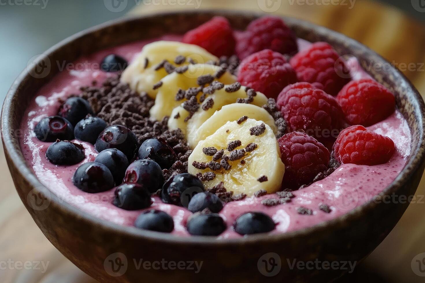 Delicious smoothie bowl with banana, raspberries, blueberries and chocolate granola topping photo