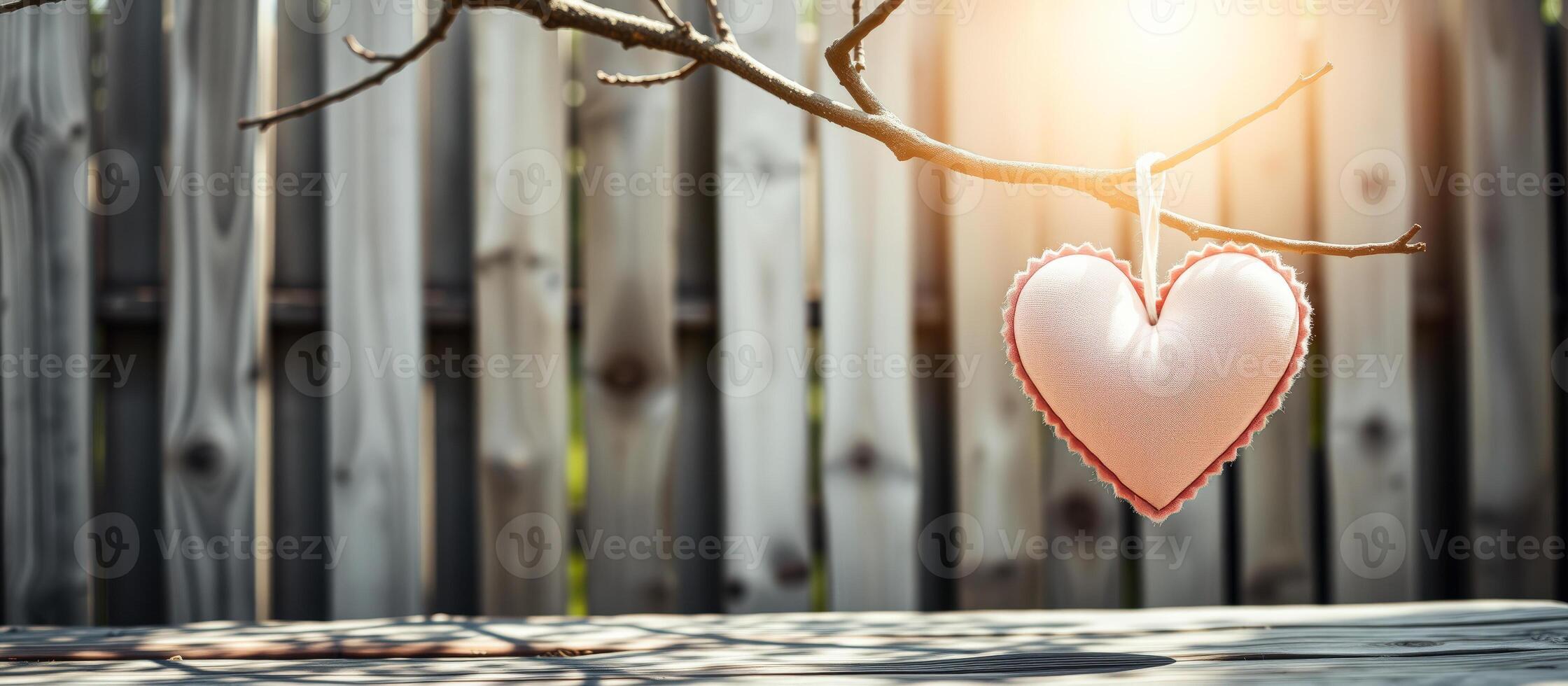 Pink heart hanging from tree branch against wooden fence photo