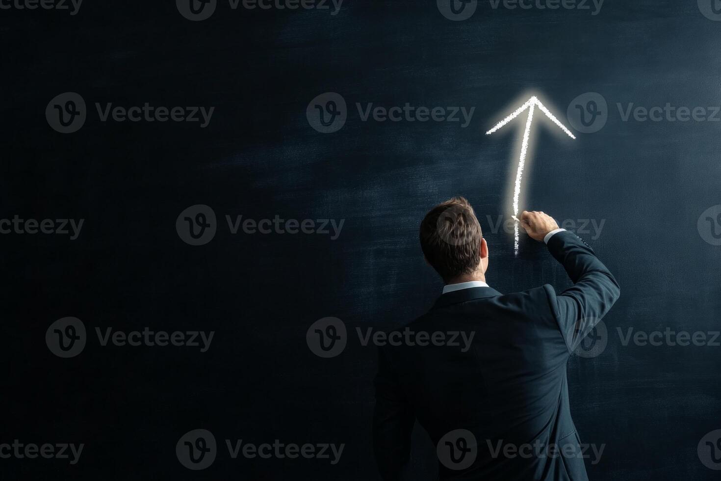A businessman in his 30s draws a glowing upward arrow on a blackboard in a dimly lit room, symbolizing leadership photo