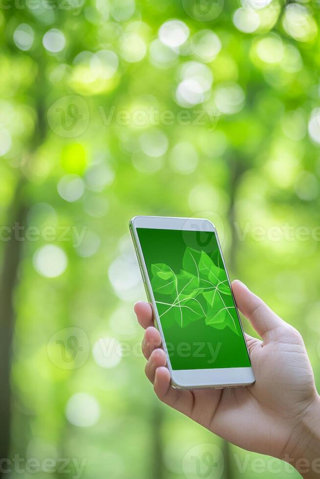 Close-up of a hand holding a smartphone with a green eco-friendly app surrounded by a lush forest backdrop photo