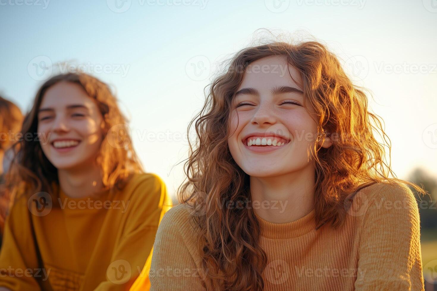Diverse youth laughing and enjoying a sunny evening at a park event while seated on the grass photo