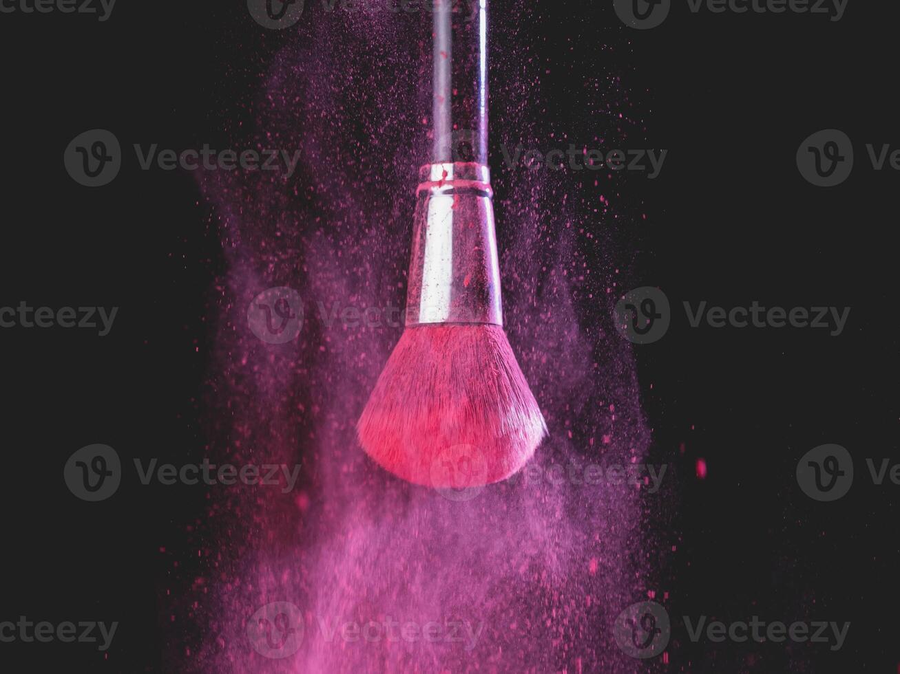 Make-up brush with pink powder splashes explosion on black background. Beauty concept photo