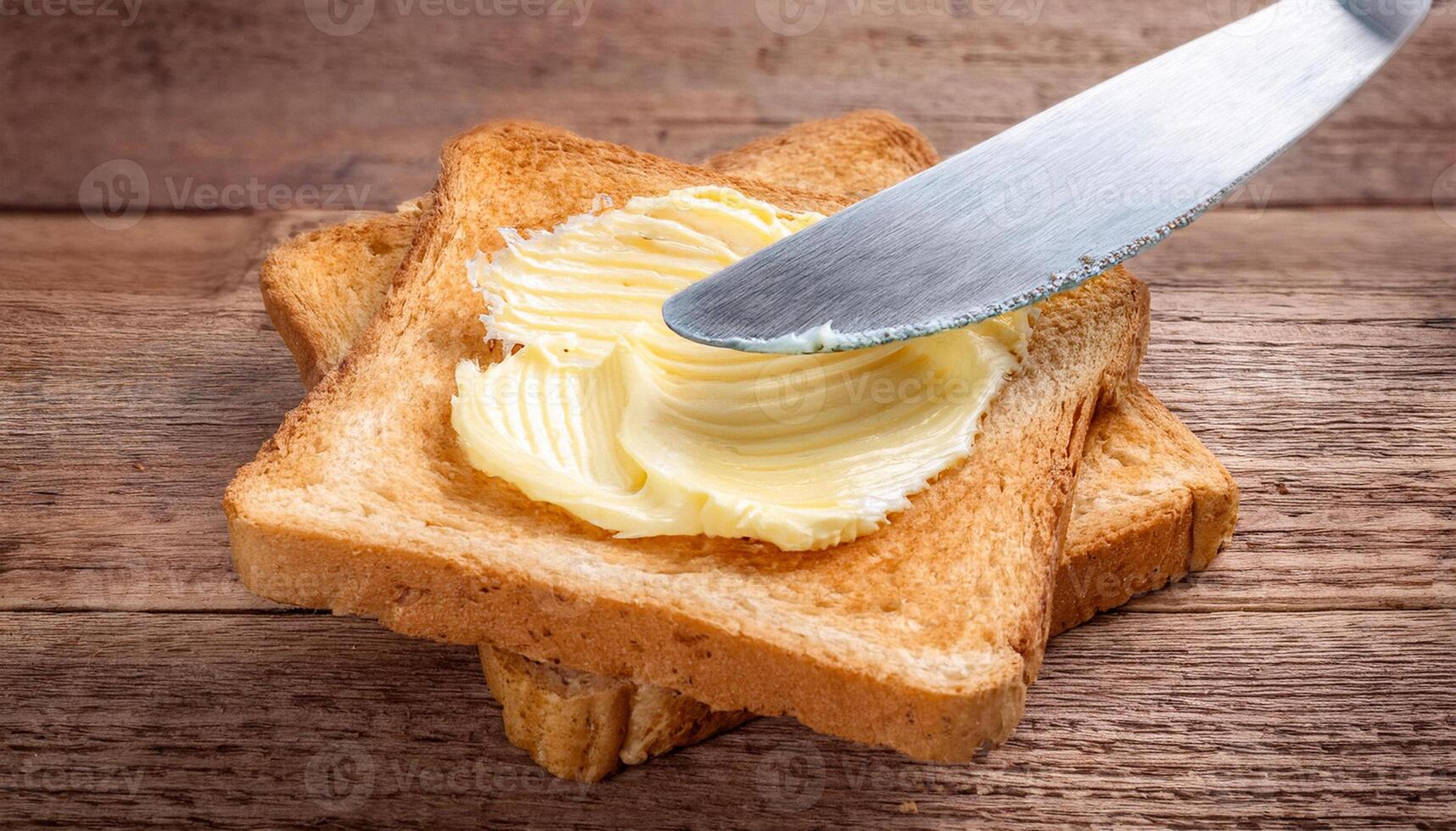 Knife spreading butter on toast bread on wooden background photo