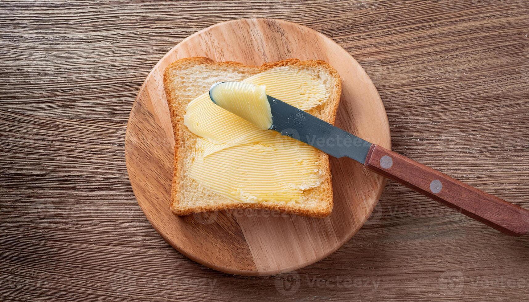 Knife spreading butter on toast bread on wooden background photo