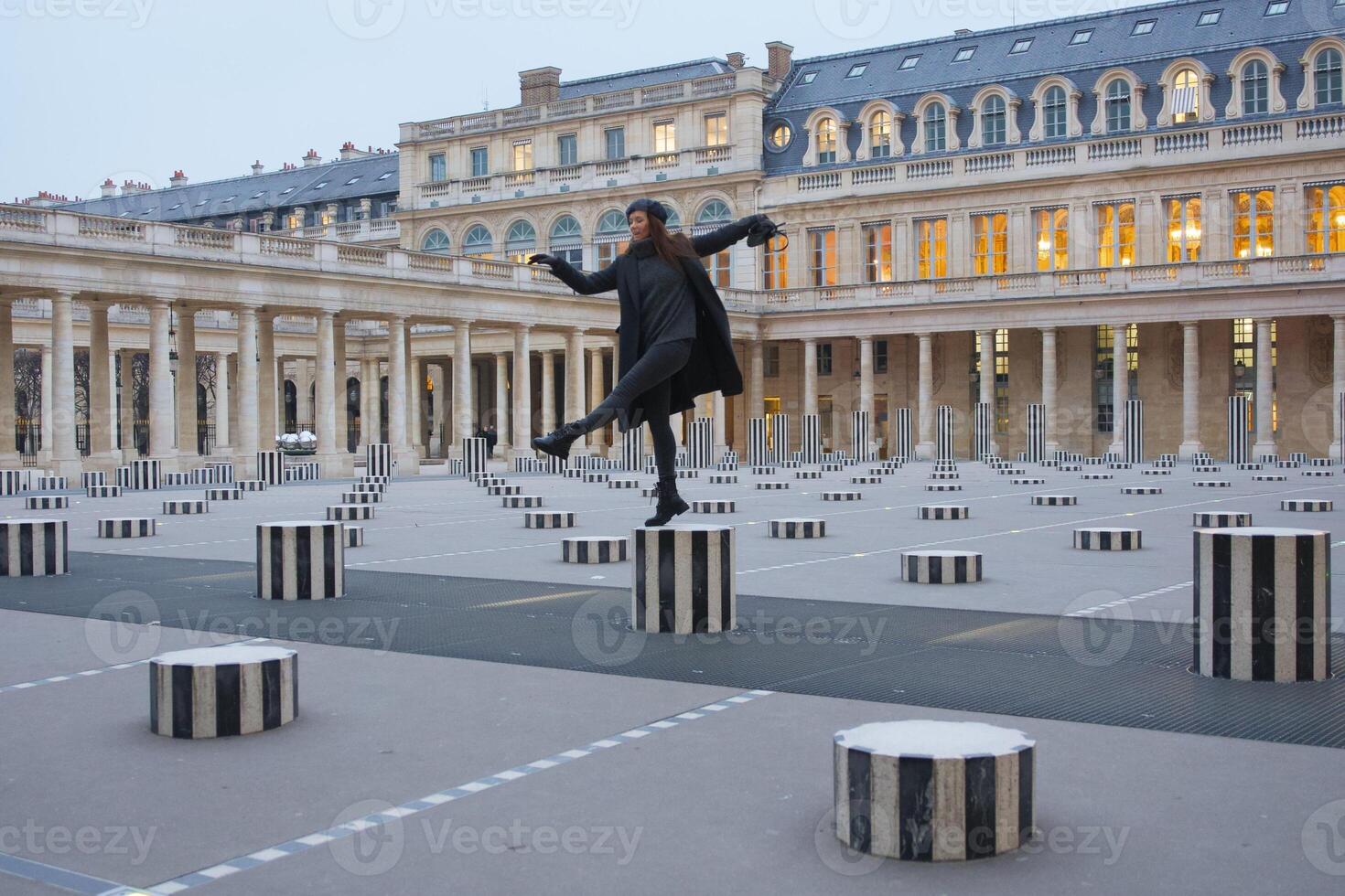 Fashionable Young Woman Balancing on Les Colonnes de Buren in Paris Courtyard photo