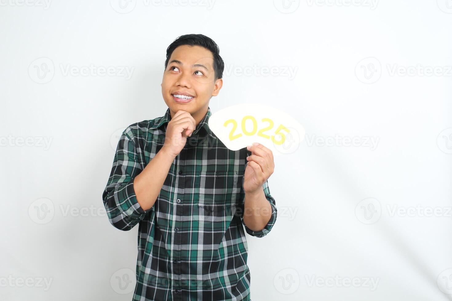 happy asian man holding 2025 new years eve greeting card with hand on chin showing thinking gesture isolated on white background photo