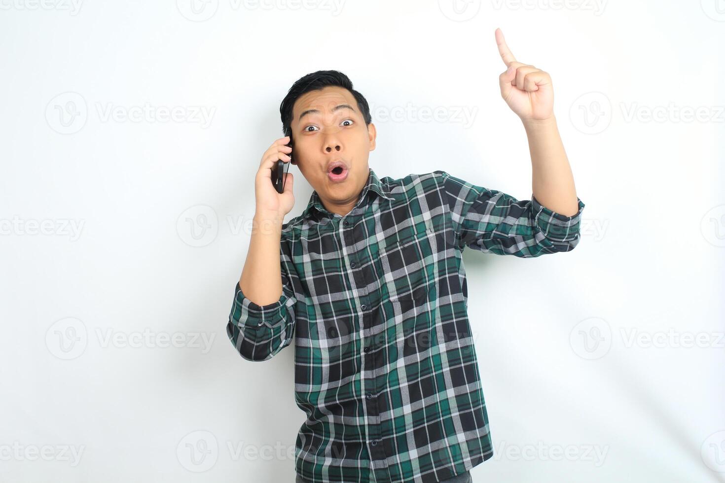 asian man pointing hand with shocked expression while talking on smartphone isolated on white background photo