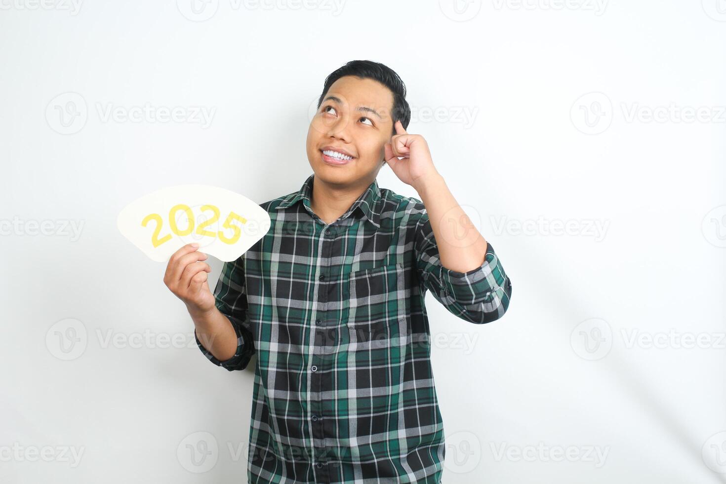 happy asian man holding 2025 new years eve greeting card with hand touching his head showing thinking gesture isolated on white background photo