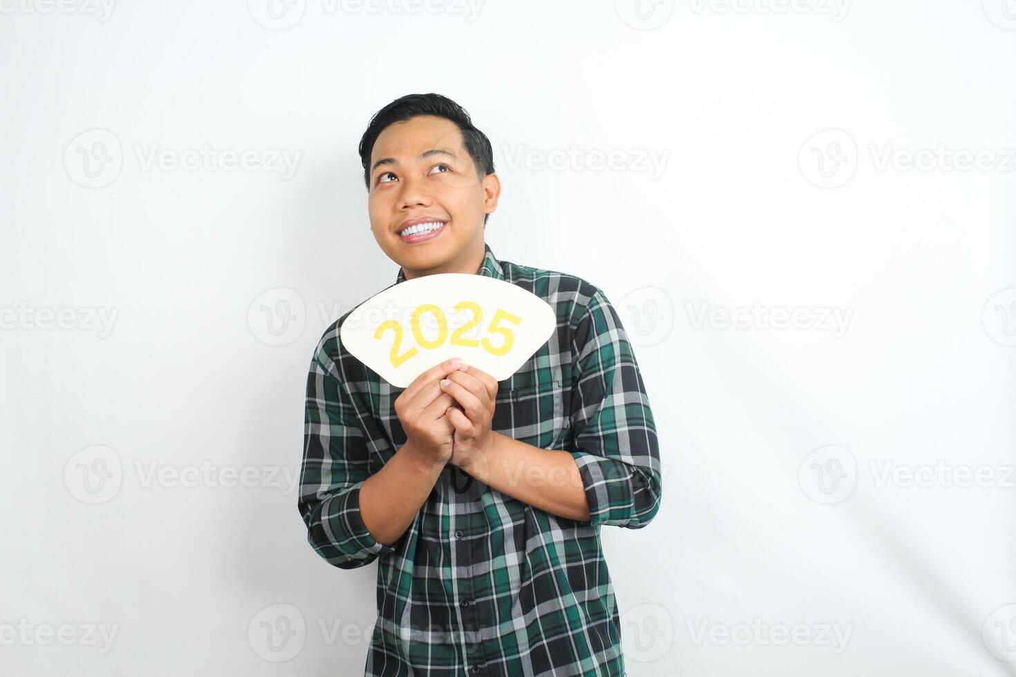 happy asian man holding 2025 new years eve greeting card and looking above showing thinking gesture isolated on white background photo
