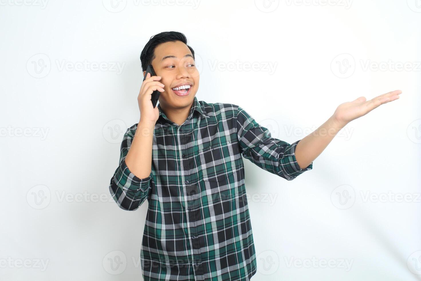 cheerful and carefree asian man wearing casual clothes presenting empty hand while talking on cellphone, calling, with smiling face isolated on white background photo