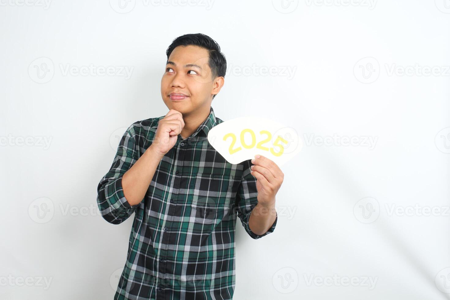 happy asian man holding 2025 new years eve greeting card with hand on chin showing thinking gesture isolated on white background photo