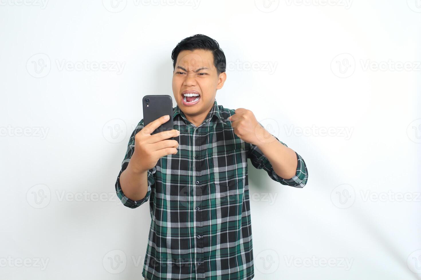 furious asian man shouting while holding cellphone and raising his hand show angry face isolated on white background photo