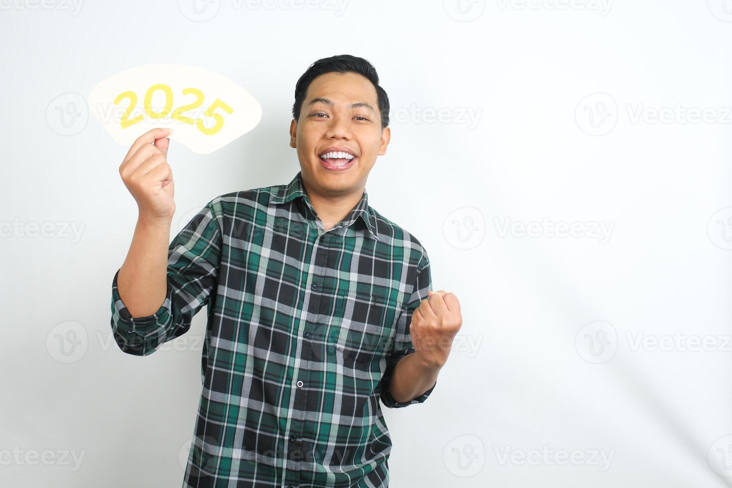 cheerful asian man holding 2025 new years eve greeting card and raising his hand showing yes gesture isolated on white background photo