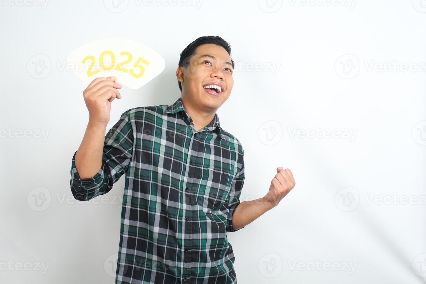 cheerful asian man holding 2025 new years eve greeting card and raising his hand showing winning gesture isolated on white background photo