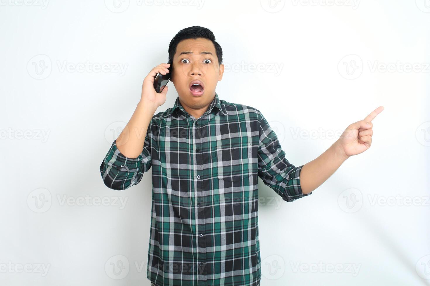 shocked asian man pointing finger while talking on smartphone isolated on white background photo