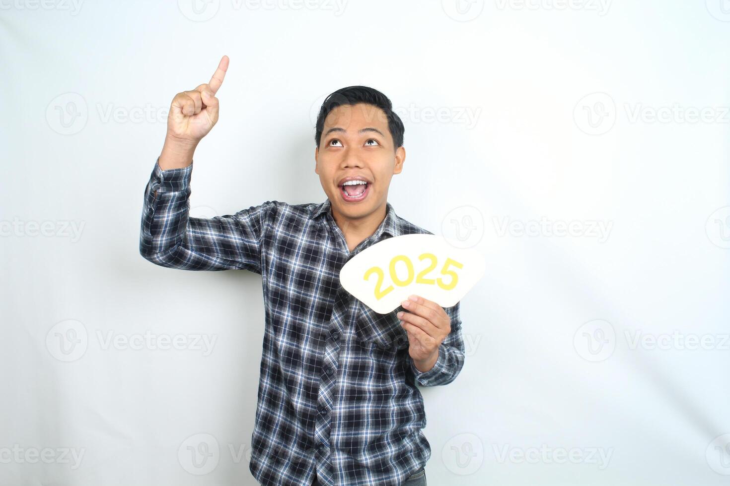 playful asian man wearing casual clothes holding 2025 new year eve greeting card pointing to above and looking up isolated on white background photo