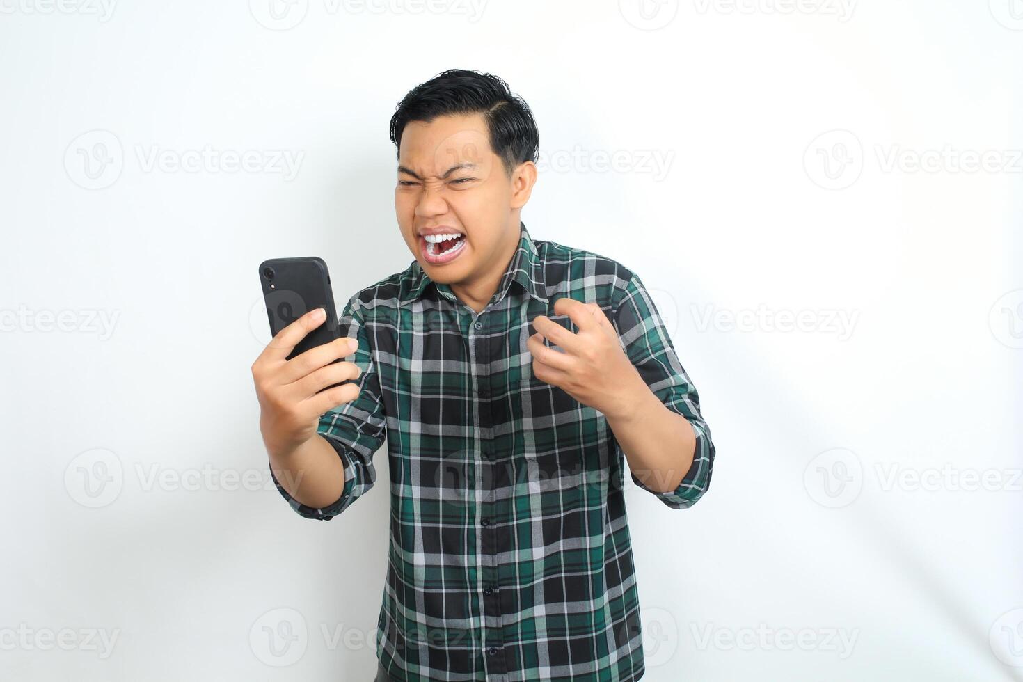 mad asian man holding cellphone raising his hand show grabbing gesture looks angry and furious isolated on white background photo