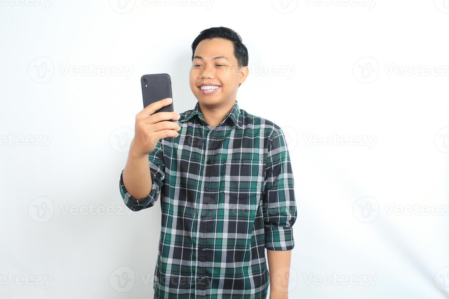 happy asian man wearing casual shirt holding cellphone read news, message, and chatting with smiling face isolated on white background photo
