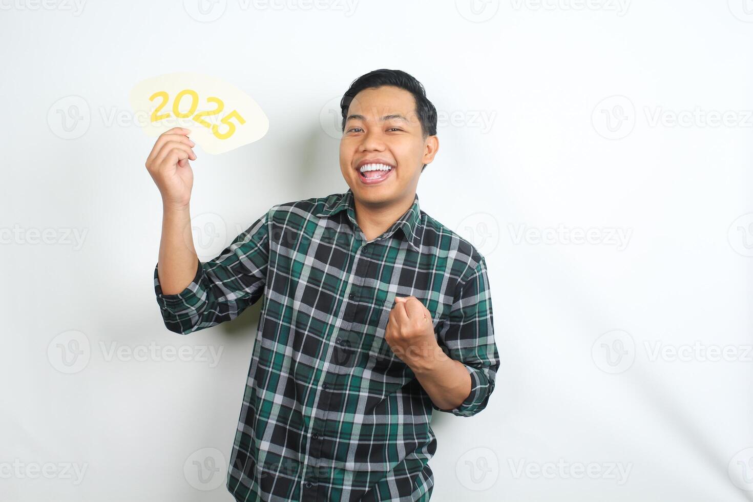 excited asian man showing victory and winning gesture while holding 2025 board isolated on white background photo