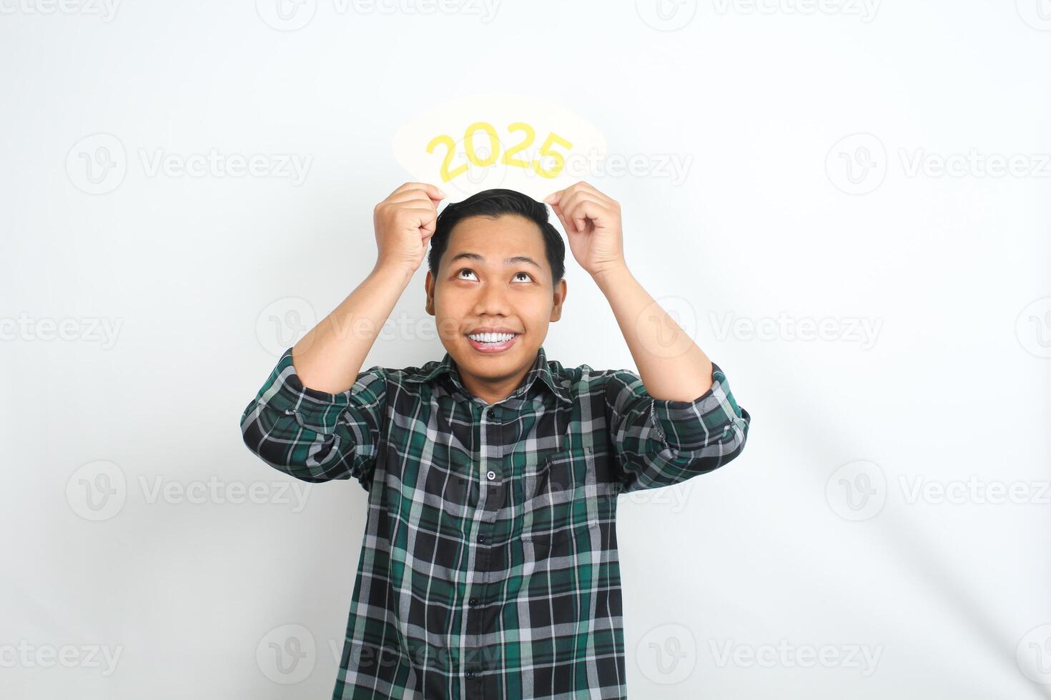 isolated happy asian man holding 2025 new year eve greeting card and looking up with smiling face wearing casual clothes photo