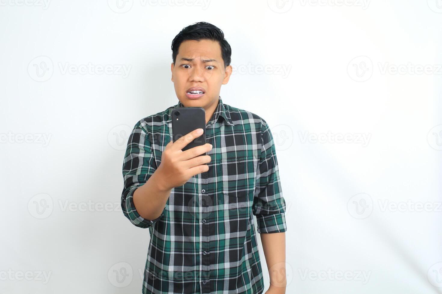 mad asian man holding cellphone and raising his hand looks angry and furious isolated on white background photo