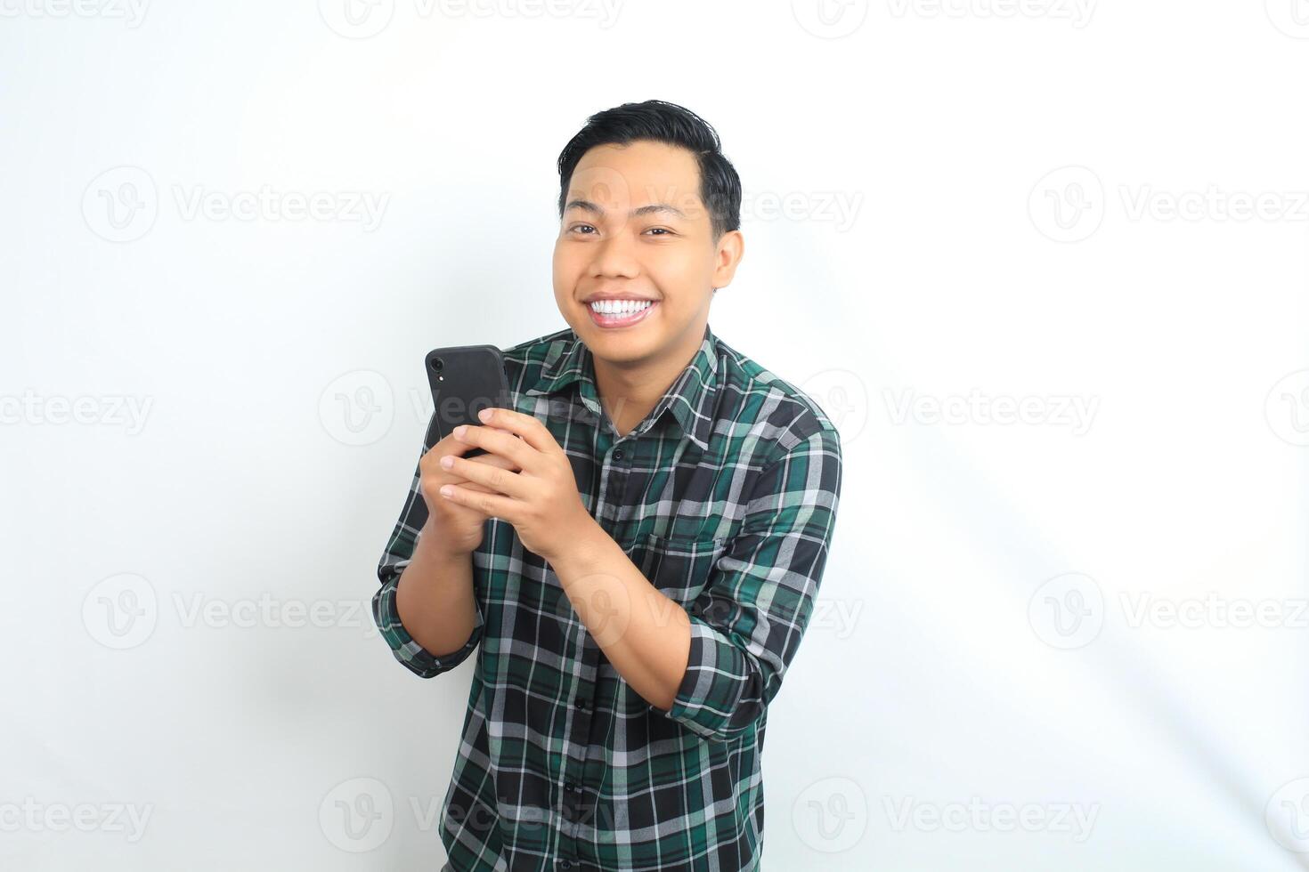 happy asian man wearing casual shirt holding cellphone read news, message, and chatting with smiling face isolated on white background photo