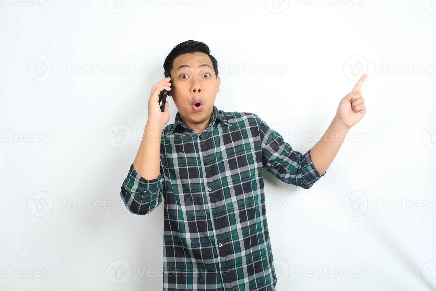 asian man pointing hand with shocked expression while talking on smartphone isolated on white background photo