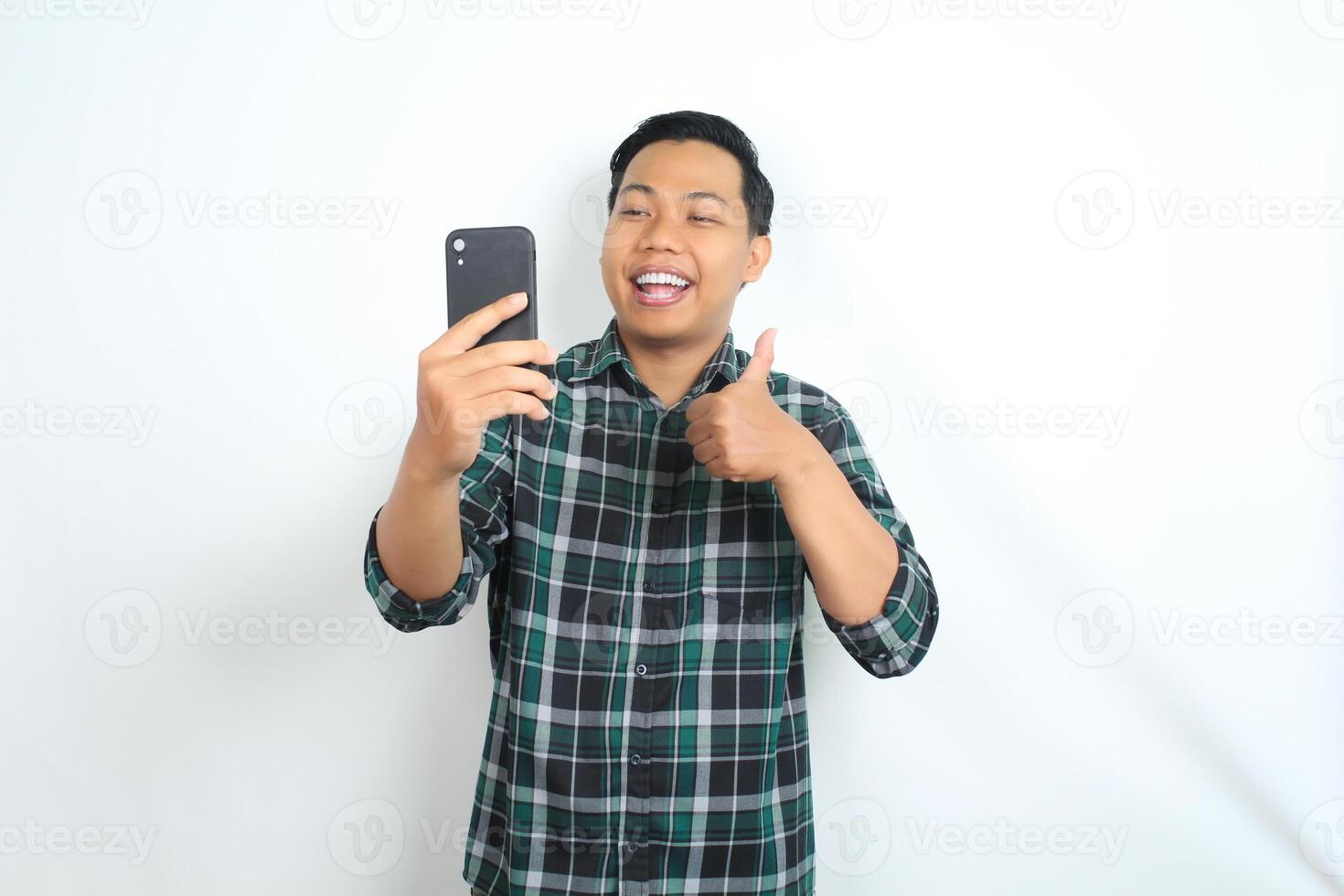 happy asian man holding mobile phone wear casual shirt show thumbs up, yes gesture, with smiling face isolated on white background photo