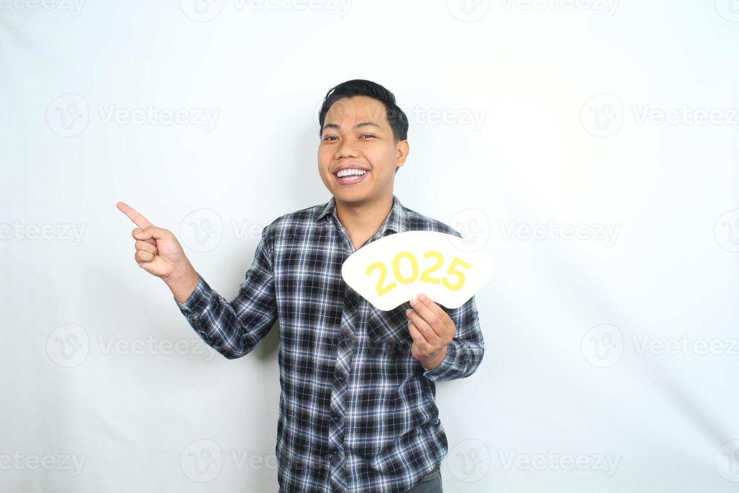 playful asian man wearing casual clothes holding 2025 new year eve greeting card pointing to copy space isolated on white background photo