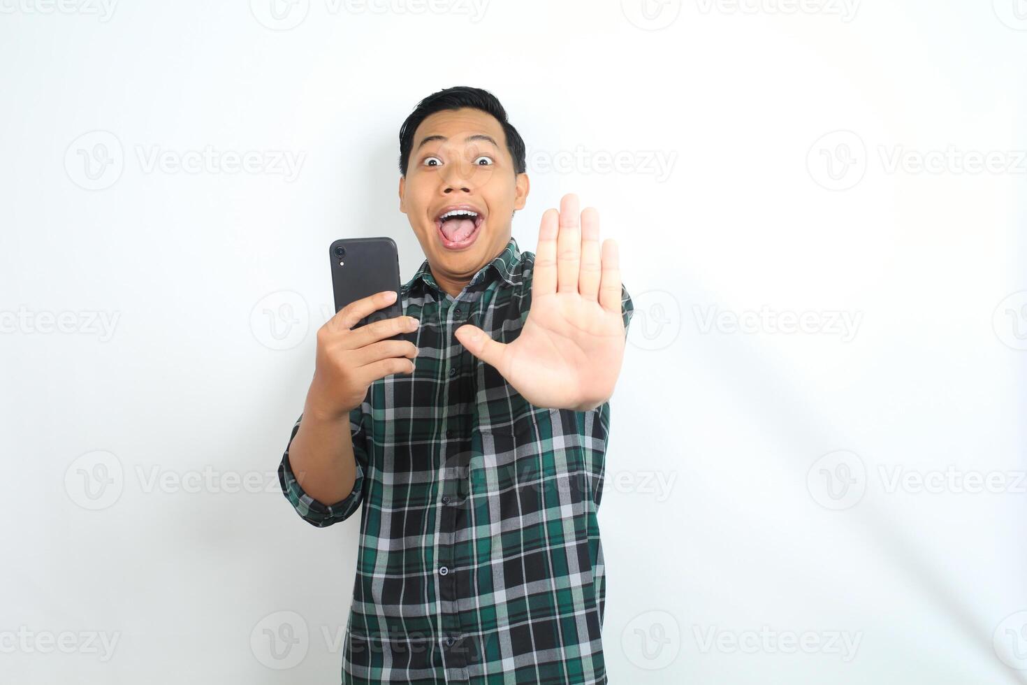 stop, asian man holding smartphone looks surprised isolated on white background, wearing casual green shirt photo