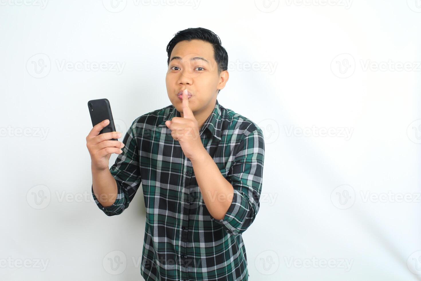 attractive and cheerful asian young man do silent gesture, be quiet, with holding smartphone wearing casual clothes isolated on white background photo