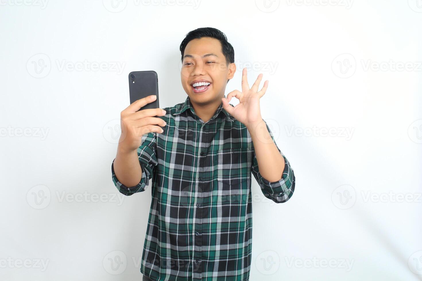 happy asian man holding smartphone wear casual shirt show ok sign, approved, yes gesture, with smiling face isolated on white background photo