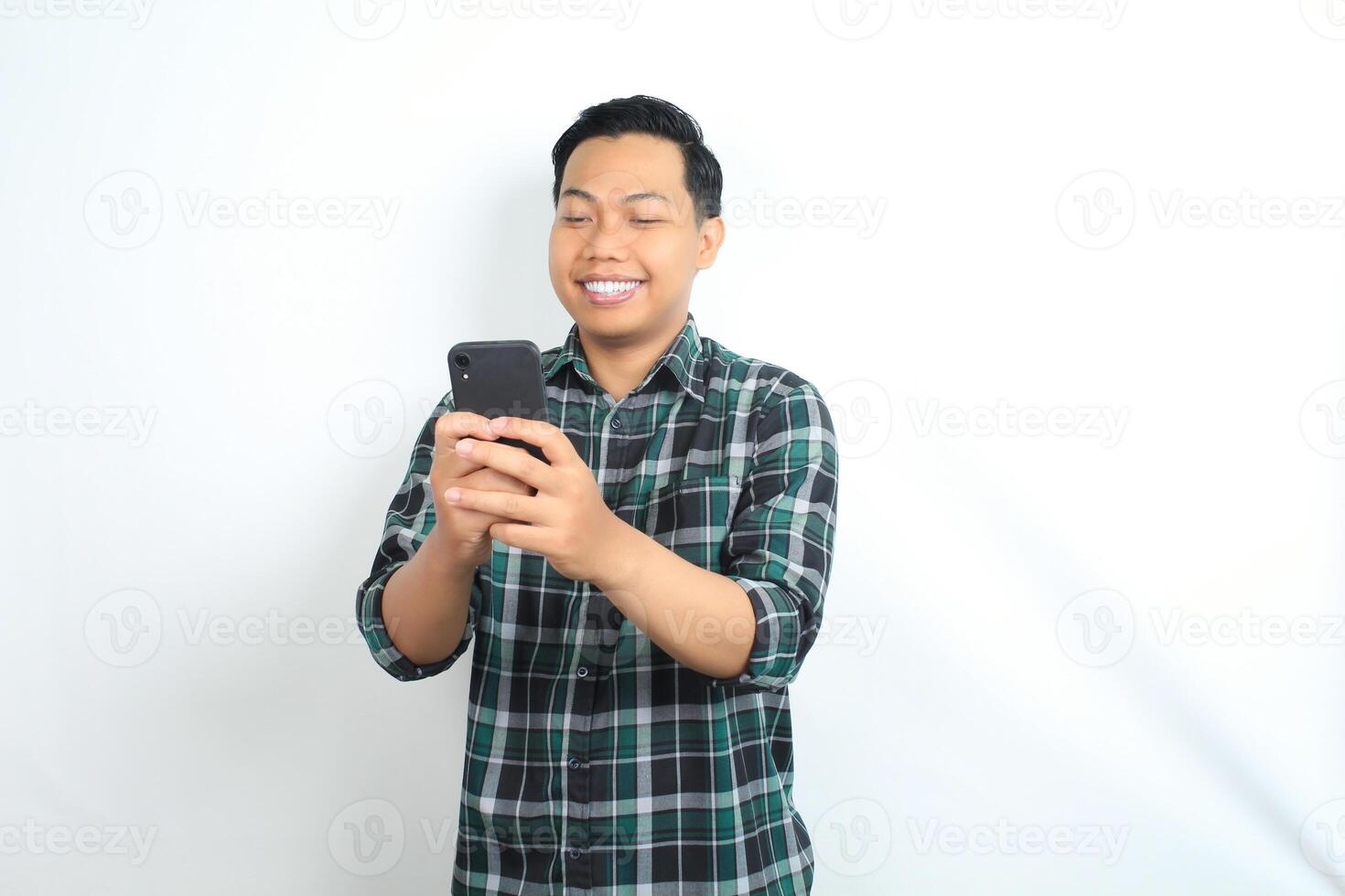 happy asian man wearing casual shirt holding cellphone read news, message, and chatting with smiling face isolated on white background photo