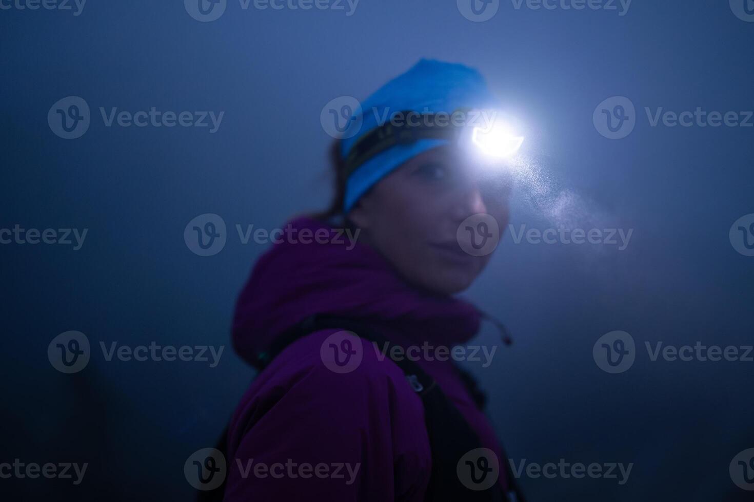female Hiker or triathlon trail runner with a headlamp on a trail in the mountain with fog at night photo