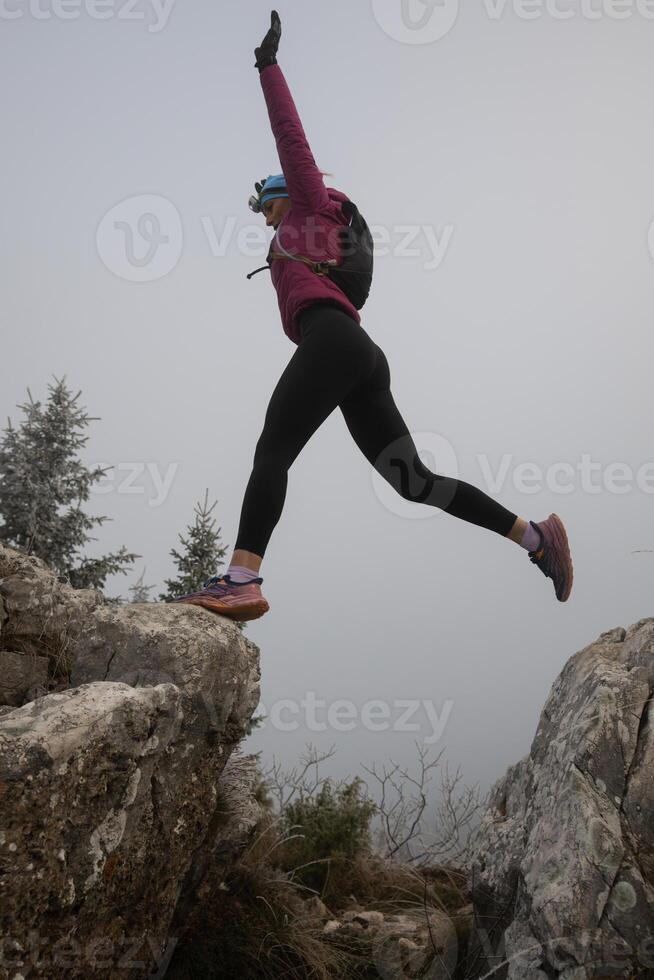 silhouette of a fitness woman trail runner jumping over a cliff and running to a rocky mountain top photo