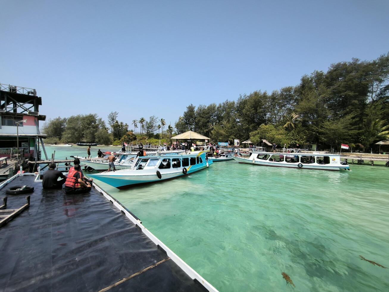 Karimunjawa, Indonesia, 2024 - Tourists relax on the boat dock enjoying the view of the clear water at the port of Menjangan Island, Karimunjawa. photo