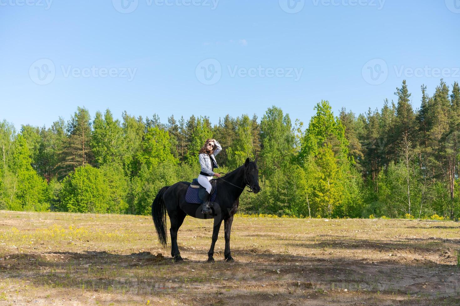 Woman is riding a horse in a field with trees in the background photo