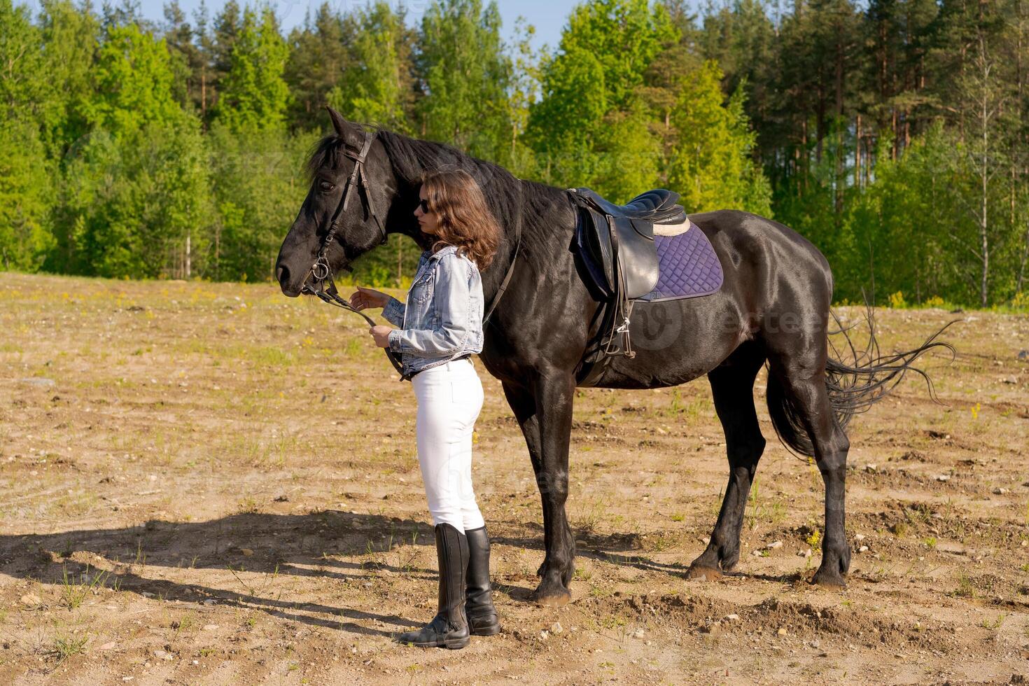 Woman is standing next to a black horse in a field photo