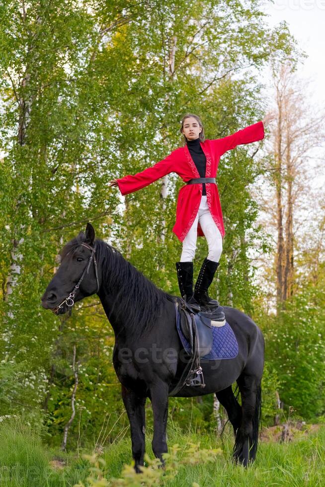 Woman is standing on top of a black horse in a forest photo