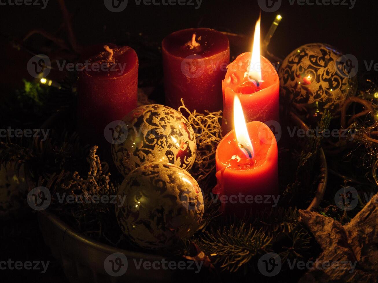 Three red candles are lit in a bowl with christmas decorations photo