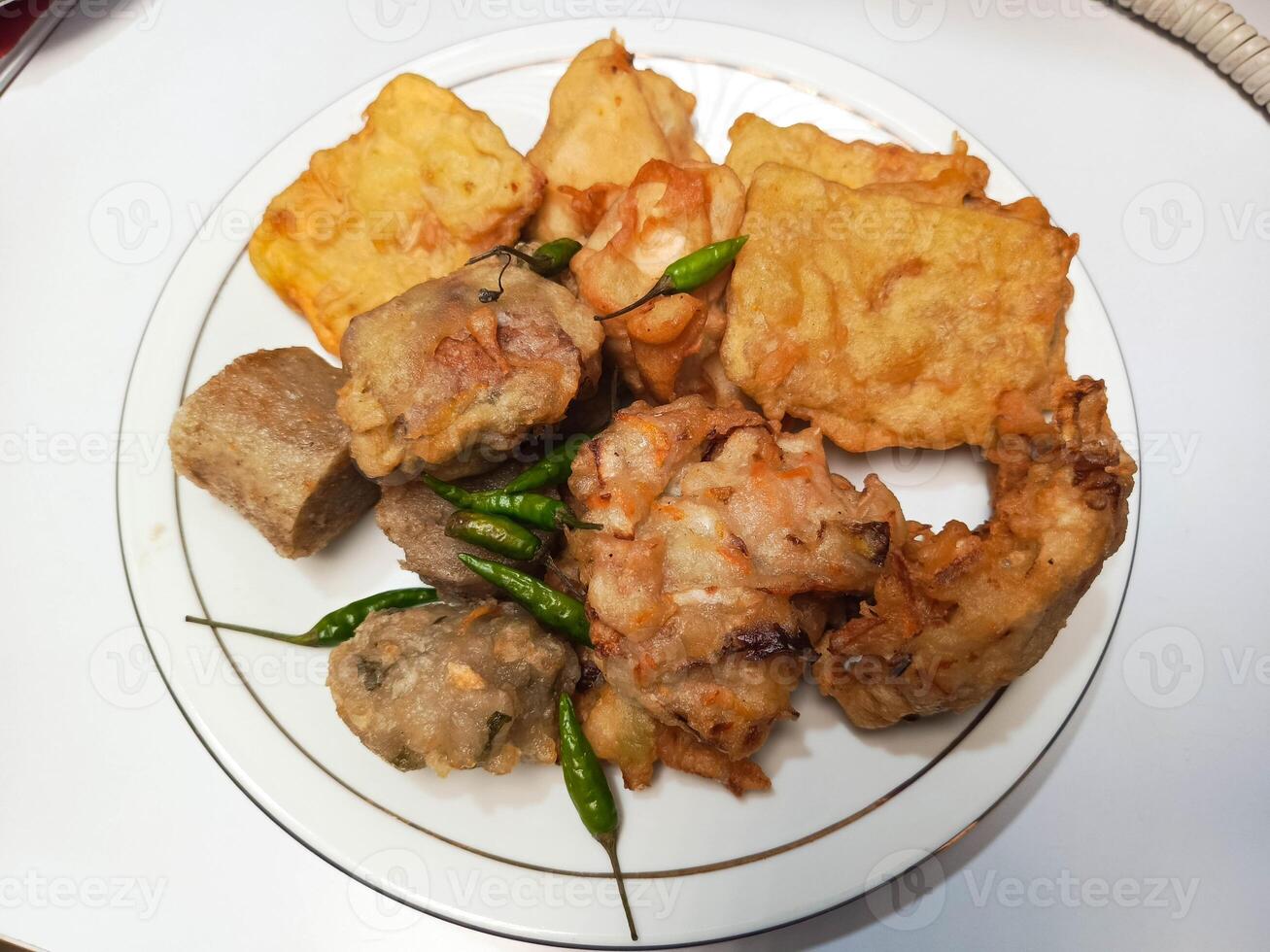 photo of a typical Indonesian snack plate consisting of fried tofu, fried tempeh, bakwan and fried banana placed on a white plate