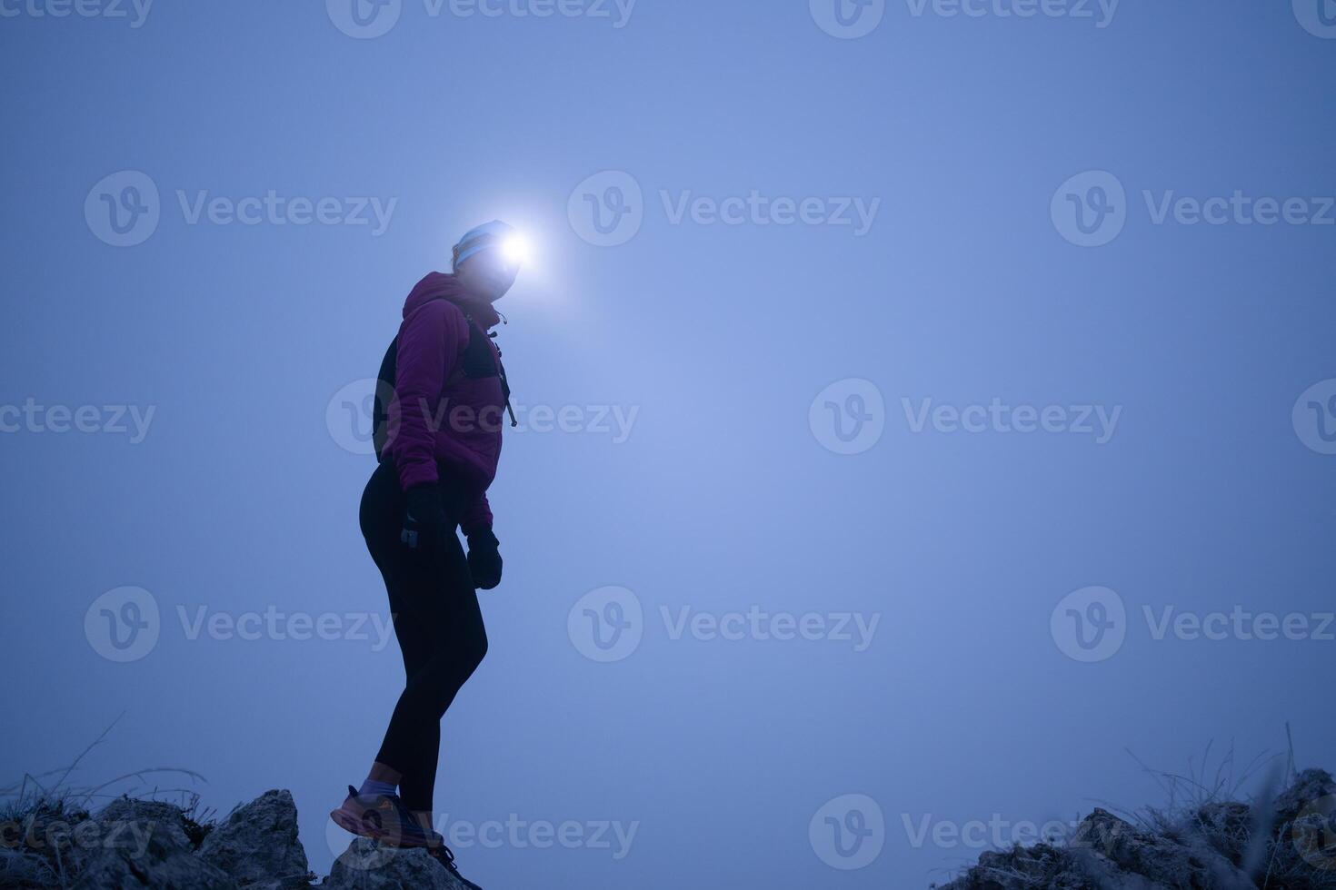 female Hiker or triathlon trail runner with a headlamp on a trail in the mountain with fog at night photo