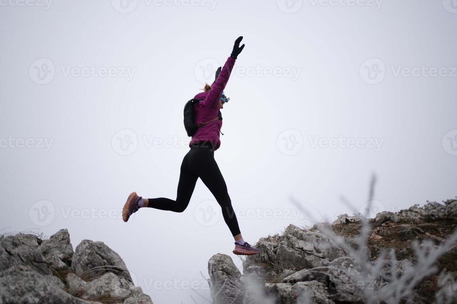 silhouette of a fitness woman trail runner jumping over a cliff and running to a rocky mountain top photo