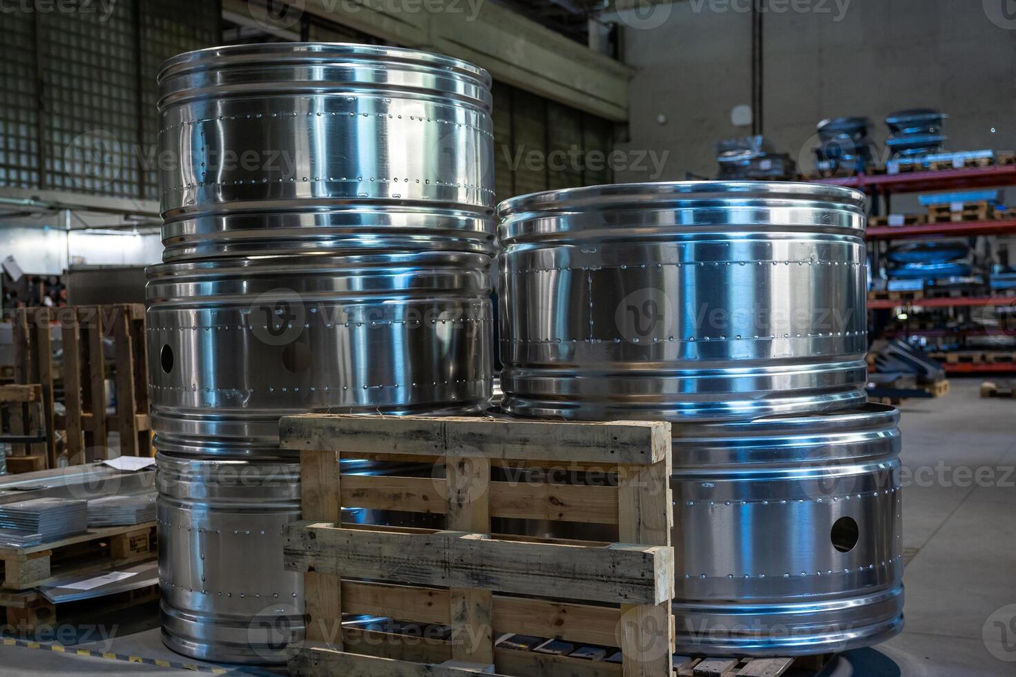 Close up of large metal cylinders stacked on wooden pallets inside a factory, emphasizing their polished surface and industrial setting. photo