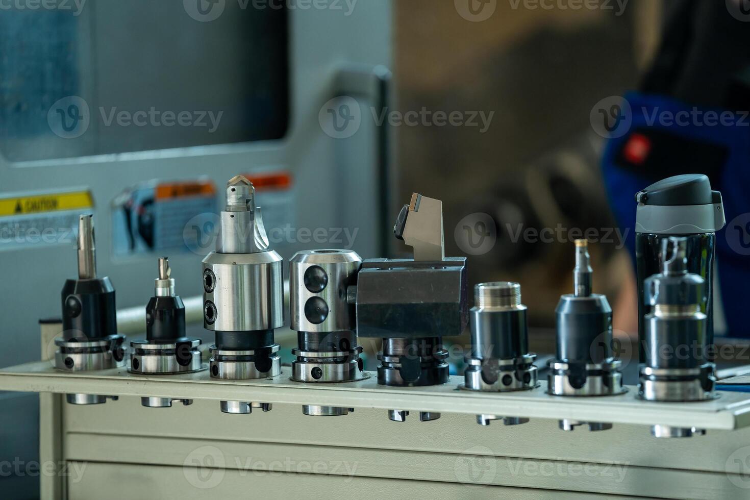 A row of various metalworking tools including drill bits and milling cutters on a workbench in a well organized metalworking factory with industrial machinery in the background. photo