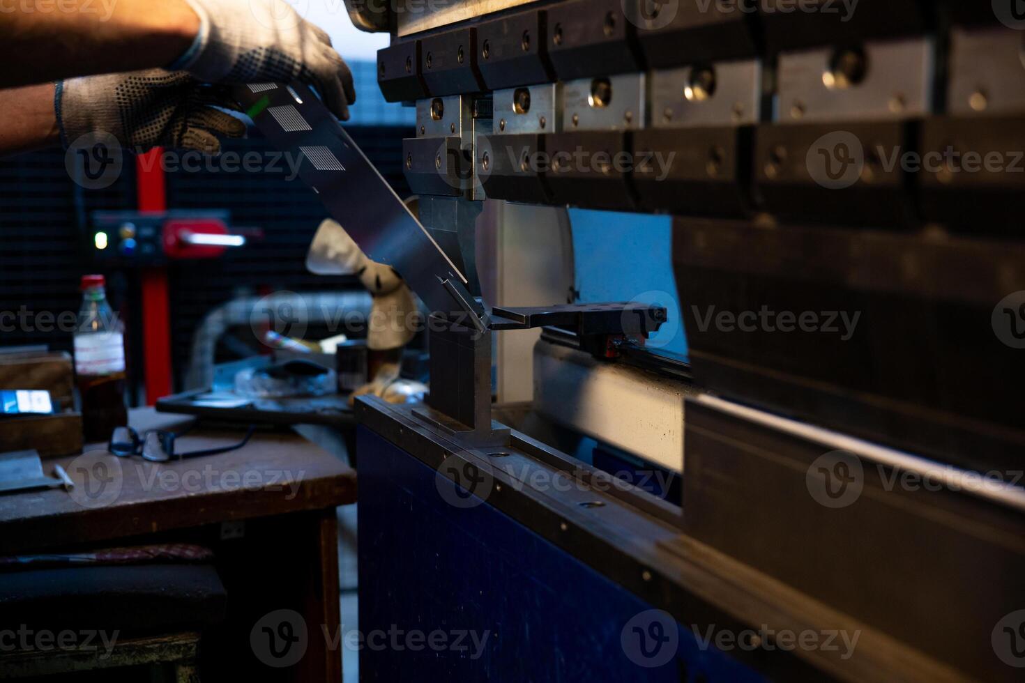 A worker's gloved hands carefully position a metal sheet into an industrial press machine, ensuring precision during the bending process. photo