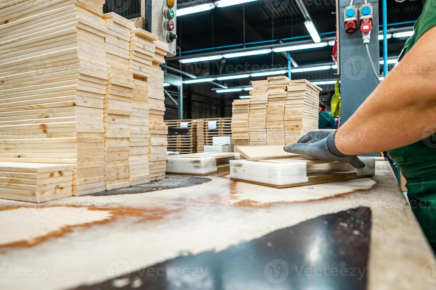Worker handling stacks of wooden planks in a woodworking factory, preparing materials for further processing under industrial lighting photo